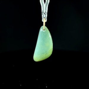 May include: A smooth, teardrop-shaped pendant in a soft, translucent seafoam green hue. The pendant features a polished surface and is suspended from a small, thin gold-toned metal jump ring, which is attached to a silver-toned metal clip.