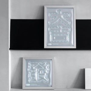 May include: Two framed prints with white frames and a white background. The prints feature Chinese characters in a 3D embossed style. The text on the prints reads "Good fortune as you wish. Wish you happiness and prosperity."