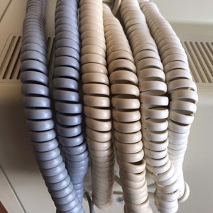 以下が含まれることがあります： 5本の電話コードが巻かれた状態のクローズアップ。2本はグレーで、3本はクリーム色です。