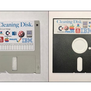 Puede incluir: Un disquete gris con una etiqueta que dice "Cleaning Disk. We Love Vintage" y presenta logotipos de Atari, Commodore, Philips e IBM. El disquete está al lado de un disquete negro con una etiqueta similar.