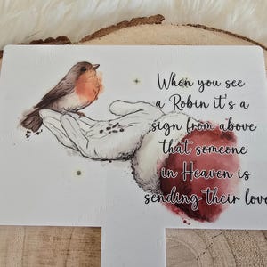 May include: A white card with a hand holding a robin and the text "When you see a Robin it's a sign from above that someone in Heaven is sending their love".