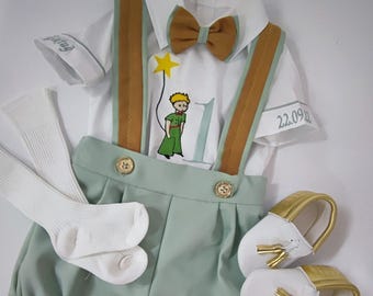 May include: A baby outfit with a white shirt, brown braces, green shorts, white socks, and gold shoes. The shirt features an embroidered image of The Little Prince and the text "22.09.20".