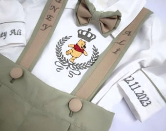 May include: A white baby outfit with a green and brown bib and braces. The bib features a Winnie the Pooh design with a crown and the text "Gönen Ali" and "22.11.2023".