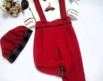Puede incluir: Un conjunto rojo y blanco para un bebé o un niño pequeño. El conjunto incluye una camisa blanca con una corbata de lazo roja, tirantes rojos, pantalones rojos y un gorro rojo con ribete de cuadros negros y rojos. La camisa tiene un coche rojo con el número 2 y el texto "2. Geburtstag" en el lado izquierdo y "Kleiner Prinz" en el lado derecho.