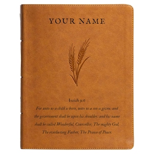 Könnte beinhalten: Ein hellbraunes, ledergebundenes Notizbuch mit dem Text "YOUR NAME" oben. Darunter befindet sich ein Weizenähren-Design und der Text "Jesaja 9,6" gefolgt von einem Bibelvers. Das Notizbuch ist geschlossen und hat einen genähten Rücken.