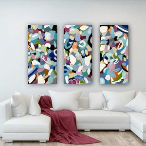 Può includere: Tre dipinti astratti in stile contemporaneo. I dipinti sono un mix di colori vivaci, tra cui blu, verde, rosa, arancione e giallo. I dipinti sono disposti in fila su una parete bianca sopra un divano bianco.