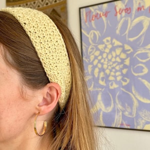 May include: A woman wearing a yellow crocheted headband and gold hoop earrings.