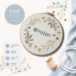 May include: A round embroidery hoop with the name "Winston" stitched in black. The design features a floral wreath with daisies, leaves, and bees. The text "PDF Embroidery Pattern" is in a circle at the top. Additional text includes "Customizable Text", "Beginner Friendly", "Step-by-Step Guide", and "Printable Template".