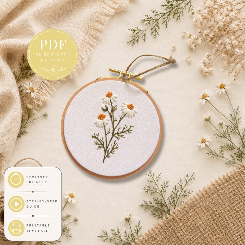 May include: A circular wooden embroidery hoop containing white fabric with a stitched design of three white daisy flowers with yellow centers and green stems. A yellow circular badge reads PDF EMBROIDERY PATTERN. A white rectangular label lists features.