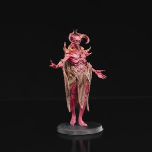Op de afbeelding: Een rood en bruin geverfd miniatuurbeeldje van een demon met hoorns en een vloeiende mantel. Het beeldje staat op een zwarte basis.