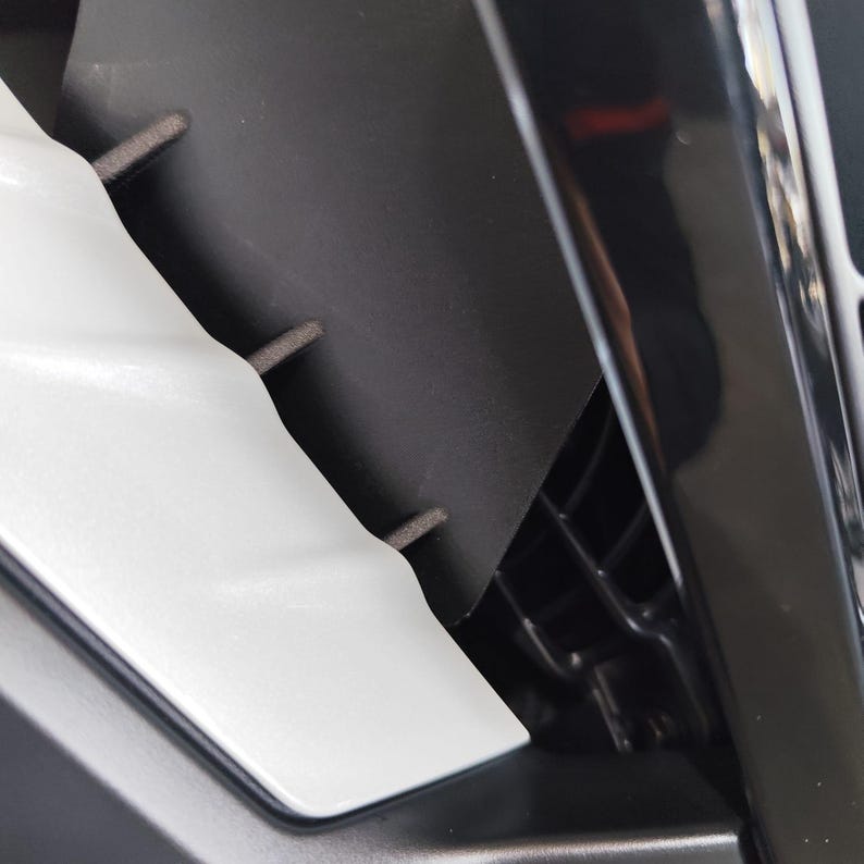 May include: Close-up of a car's interior, featuring a white plastic component with a curved design, set against a black background. The image highlights the contrast between the white and black elements, showcasing the car's design.