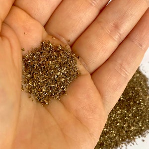 Może przedstawiać: Zbliżenie na stos błyszczących, złotych wiórków metalowych w dłoni osoby. Wiórki są małe i o nieregularnym kształcie, a mają metaliczny połysk.