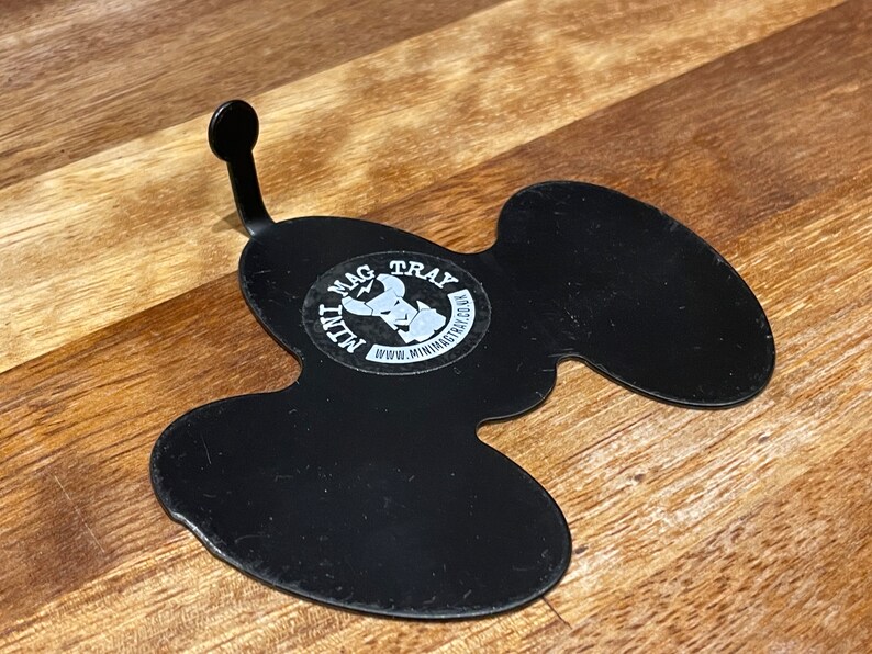 Puede incluir: Bandeja de metal negro con una forma &uacute;nica y un asa curvada. La bandeja tiene una pegatina circular con el texto "MAG TRAY" y un gr&aacute;fico. Tambi&eacute;n es visible la direcci&oacute;n del sitio web "www.minimagtray.co.uk".