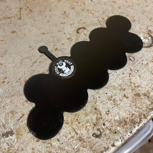 May include: Black metal tray with a unique cloud-like shape. The tray features a small handle and a circular sticker with the text "MINI MAG TRAY" and a graphic. The tray is designed to hold small items.