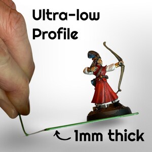 May include: A miniature archer figurine in a red and white outfit, holding a bow. The text "Ultra-low Profile" and "1mm thick" are displayed. A hand holds a thin green line, demonstrating the product's profile.