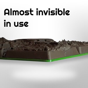 May include: A dark brown, textured object with a green base. The text "Almost invisible in use" is displayed in black letters above the object. The object appears to be a miniature landscape or terrain piece.