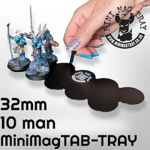 May include: A black MiniMagTAB-TRAY holds three miniature figurines. The tray is held by a hand with long, blue fingernails. The figurines are blue and gold, with detailed armor. Text on the tray reads "32mm 10 man MiniMagTAB-TRAY".