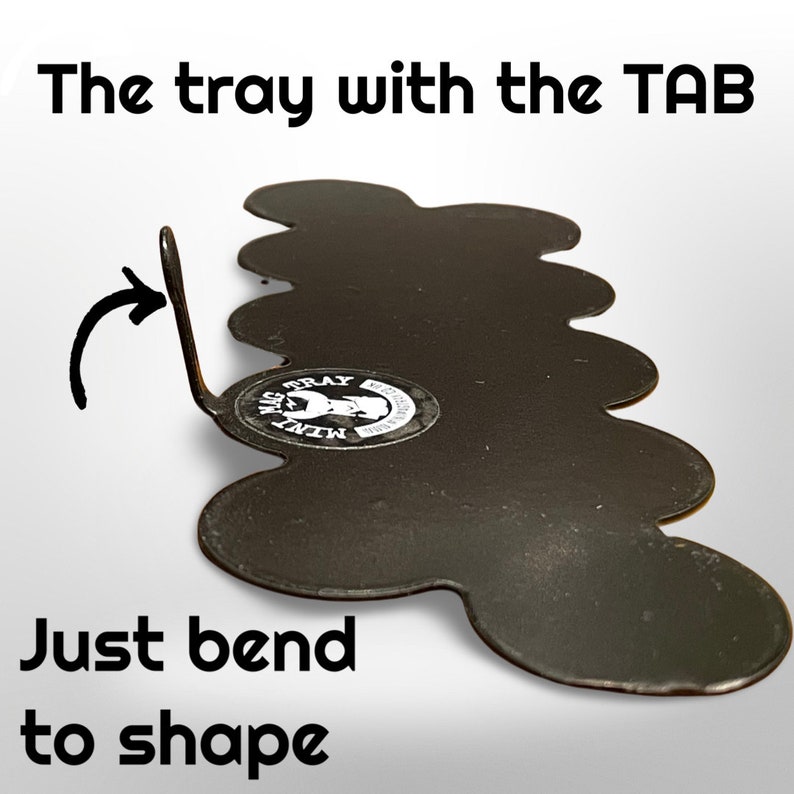 May include: A black metal tray with a tab, shaped with a wavy edge. The text "The tray with the TAB" and "Just bend to shape" are visible. A sticker with text and a graphic is on the tray.