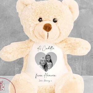 May include: A beige teddy bear with a white heart-shaped patch on its chest. The patch has a black and white photo of two people inside the heart and the text "A Cuddle from Heaven Love Nanny x".