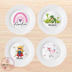 May include: Four white ceramic plates with personalised designs. The plates feature a rainbow with a heart, a group of dinosaurs, a superhero, and a unicorn. Each plate has a name written below the design: Amelia, Reuben, Dennis, and Rosie.