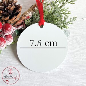 K&ouml;nnte beinhalten: Ein wei&szlig;er, runder Weihnachtsschmuck mit rotem Band. Der Anh&auml;nger misst 7,5 cm im Durchmesser und zeigt den Text "7,5 cm" in Schwarz. Festliches Gr&uuml;n und rote Beeren umgeben den Anh&auml;nger.