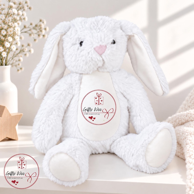 May include: A white plush rabbit toy with long floppy ears and a soft textured finish. The center of the chest features a circular graphic with a gift box icon, three small hearts, and the text Gifty Woo A little love from me to you.