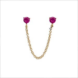 Puede incluir: Un par de pendientes dorados con dos gemas redondas de color rosa brillante conectadas por una delicada cadena. Los pendientes están sobre un fondo blanco, resaltando el diseño y el color de la joyería.