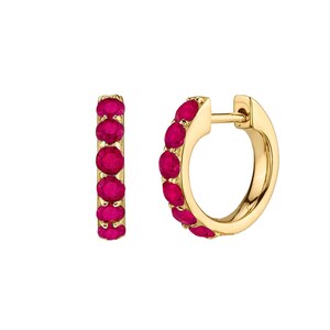 May include: A pair of gold hoop earrings, each adorned with a row of vibrant, oval-cut ruby gemstones. The earrings have a polished, reflective surface, and the rubies are a deep, rich red color. The design is simple yet elegant.