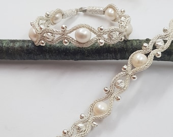 May include: Two silver bracelets with white pearls. The bracelets are made of a woven silver cord with small silver beads. The pearls are evenly spaced along the bracelets.