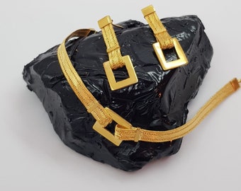 May include: A gold chain necklace and matching earrings with a square link design. The jewelry is displayed on a black surface.