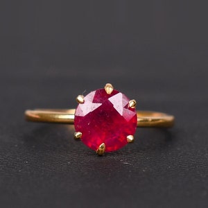 May include: A gold ring featuring a large, round, red ruby gemstone.