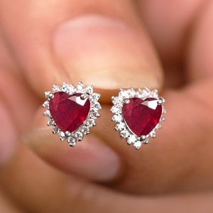 May include: A pair of heart-shaped ruby earrings with a diamond halo setting.