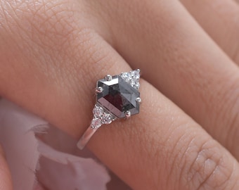 Könnte beinhalten: Ein silberner Ring mit einem schwarzen, quadratischen Edelstein, der von kleineren weißen Edelsteinen umgeben ist.