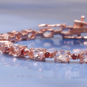 May include: A rose gold bracelet with alternating clear and red gemstones. The bracelet has a lobster claw clasp.
