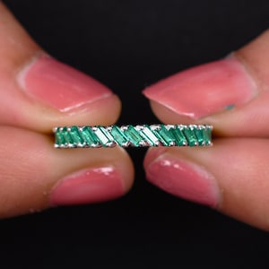 May include: A silver band ring with a row of emerald green baguette-shaped stones.