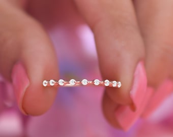 May include: A delicate rose gold band ring with a row of small, clear round diamonds.