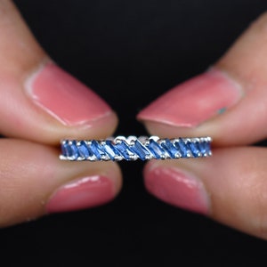 以下が含まれることがあります： 青いバゲット型のサファイアが並んだシルバーのバンドリングです。