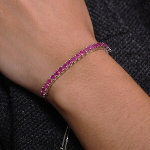 May include: A pink gemstone tennis bracelet with a silver clasp. The bracelet is adjustable with a sliding knot.