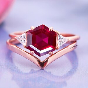 May include: A rose gold ring with a hexagonal ruby gemstone and two smaller triangular diamonds on either side. The ring has a V-shaped band.