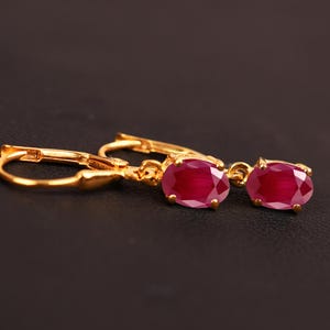 May include: A pair of gold earrings with oval-shaped ruby gemstones. The earrings have a simple design and are perfect for everyday wear.