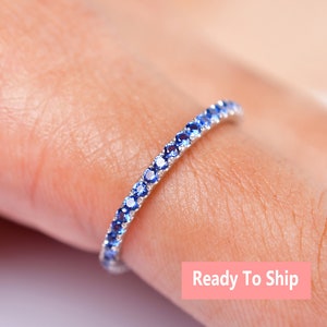 May include: A delicate eternity band ring with a row of small, sparkling blue sapphires set in a silver band.  Ready To Ship.