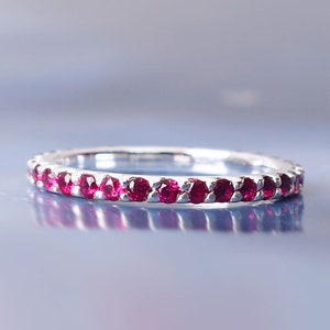 Puede incluir: Un anillo de banda de plata con una fila de pequeñas piedras de rubí rojo oscuro engastadas alrededor de toda la banda.