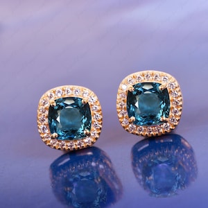 May include: A pair of gold earrings with blue gemstones surrounded by a halo of smaller clear gemstones.