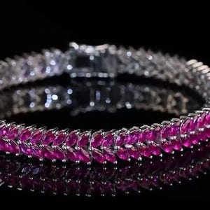May include: A silver bracelet with a row of pink marquise-shaped gemstones. The bracelet is on a black background.
