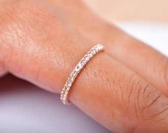 May include: A delicate rose gold band ring with a row of small, clear diamonds encircling the band.
