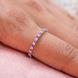 May include: A delicate eternity band ring with a row of small pink and white gemstones.