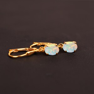May include: A pair of gold earrings with oval-shaped opal stones. The earrings have a simple design and are perfect for everyday wear.
