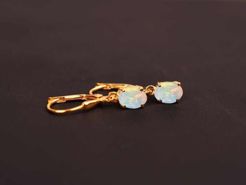 May include: A pair of gold earrings with oval-shaped opal stones. The earrings have a simple design and are perfect for everyday wear.