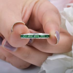 May include: A silver band ring with a row of emerald green rectangular gemstones.