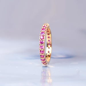 May include: A gold band ring with a row of pink gemstones.